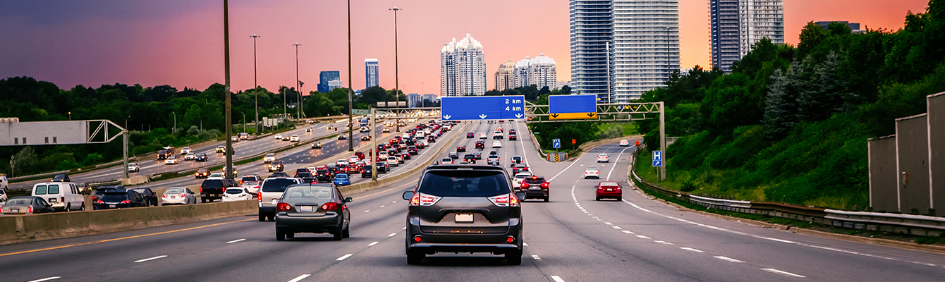 Vehicles running on unleaded fuel driving down multi-lane Canadian highway at sunset.